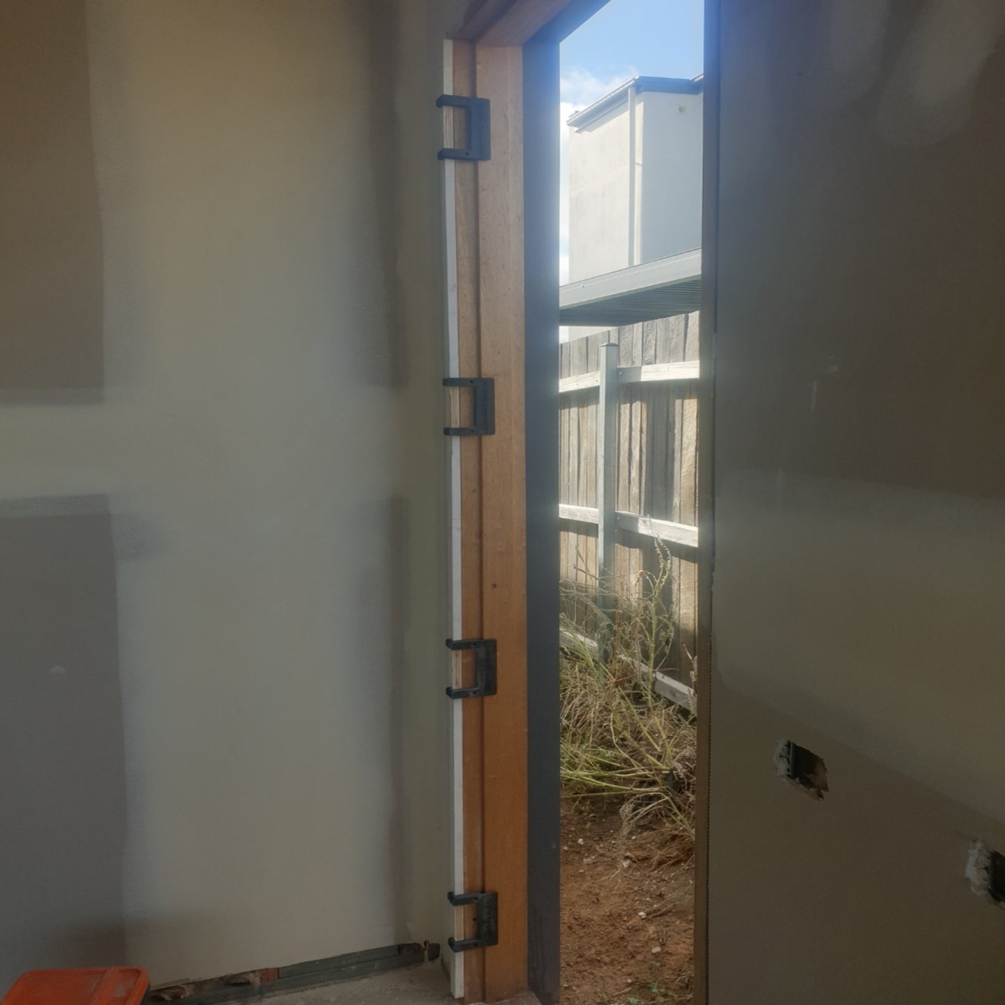 Carpenter using a modular hinge routing jig to cut a precise hinge recess in a timber door with a router.